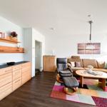 Wohnzimmer mit Sofa, Sessel, Tisch und Regal. Teppich und Wandbild sichtbar.