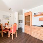 Essbereich mit Holztisch, Stühlen und Küchenbereich im Hintergrund.