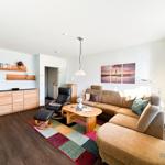 Wohnzimmer mit Sofa, Sessel und Holzmöbel. Wandbild zeigt Leuchtturm.