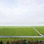 Weitläufiger Grünstreifen mit Blick auf Meer und Hafenbecken.