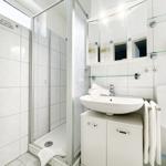 Badezimmer mit Dusche, Waschbecken und Toilette. Weiße Fliesen und Spiegel.