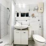 Badezimmer mit Dusche, Waschbecken und Toilette. Weiße Fliesen und Spiegelschrank.