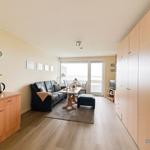 Wohnzimmer mit Sofa, Esstisch und Balkon. Holzoberflächen und große Schränke.