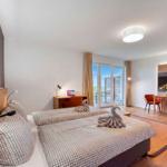 Zwei Betten mit Handtüchern als Schwäne, Schreibtisch, Fernseher und Balkon mit Sicht auf Grün.