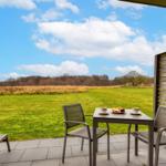Terrasse mit Tisch, zwei Stühlen und Blick auf grünes Feld und Wald.