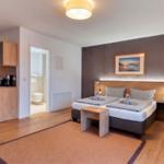 Zimmer mit Bett, Schreibtisch, Bad und Küchenbereich.