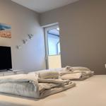 Ein Schlafzimmer mit Bett, Fernseher und Fenster. Wände sind hell, Bilder und Vogel-Dekoration sind sichtbar.