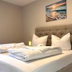 Ein Bett mit weißer Bettwäsche und einem braunen Kopfteil. An der Wand hängt ein Strandbild.