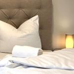 Bettkopfteil mit Knopfstickerei, zwei Kissen, eine Decke und eine Lampe.