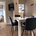 Essbereich mit Tisch, vier Stühlen und Fernseher. Im Hintergrund Schlafzimmer mit Bett.