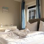 Ein Bett mit weißer Bettwäsche, Kissen und Handtüchern. An der Wand hängt ein Bild mit der Aufschrift Relax.