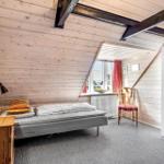 Bedroom with wooden walls, bed, chair, and wardrobe under sloped ceilings.