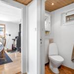 Bathroom with toilet and sink. In the background, the dining room with table and chairs is visible.