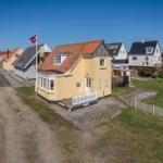 Yellow house with red roof, white fence, and garden. Other houses are nearby.