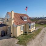 Yellow house with red roof and Danish flag. Surrounded by grass and an unpaved path.