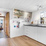 Kitchen with white cabinets, wooden floor, and window. Passage to dining area.