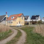 Yellow house with red roof and white windows. Other houses are behind it.