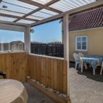 Terrace with table, chairs, and view of yellow house with roof.