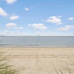 Beach with sand and gentle waves under blue sky with white clouds.