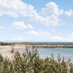 Beach with rock breakwater and green vegetation under blue sky with white clouds.