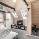 Bedroom with sloped ceiling, TV, and windows. Wooden walls and simple furnishings.