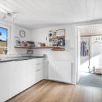 Kitchen with white cabinetry, wooden floor, and window. Passage to an adjacent room.