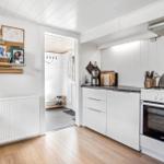 Kitchen with white cabinets, stove, and exhaust hood. Passage to another room.