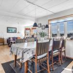 Dining room with table and chairs, view into living room with sofa and windows.