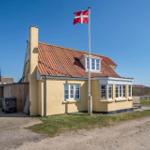 A yellow house with a red roof and a Danish flag in the foreground.