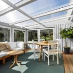 Terrace with seating area, dining table, and plant under glass roof.