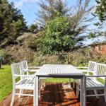 Bright terrace with white table and chairs. Greenery and trees in the background.