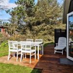 Deck with white table and chairs, wooden floor, adjacent garden and trees.