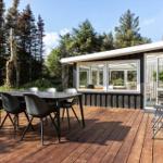 Deck with table and chairs, adjacent to a wooden cabin with glass front.