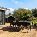 Deck with table and chairs, adjacent to house with garden and trees.