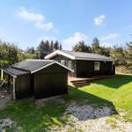 A dark-clad house with a terrace and extension. Surrounded by grass and trees under a blue sky.