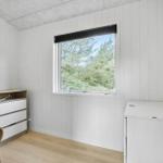 A room with white paneled walls, a window overlooking trees, and a dresser.