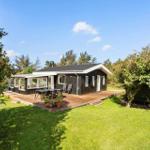 A black-clad house with a terrace and garden. Tables and chairs are outside.
