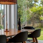 Dining table with chairs, wine bottle and glasses by large window with view of green.