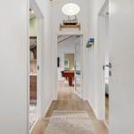 Hallway with wooden floor and rug, view into bedroom and game room with table.