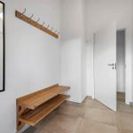 Entrance with wooden bench, mirror, and hook rack. White walls and door.