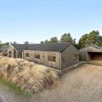 Modern wooden house with garage and grassy hill in the background.