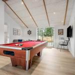 Billiard table with red felt, TV, and seating area in a bright room with wooden floor and sloped ceiling.