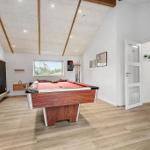 Room with pool table, wooden floor, and window. A large TV is mounted on the wall.
