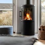 A black wood stove burns in the living room. Outside, tall grasses and a window are visible.