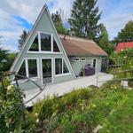 A-Frame-Haus mit Terrasse und Garten. Umgeben von Bäumen und Sträuchern.