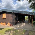 Holzhaus mit überdachter Terrasse, Grillplatz und Holzstapel.