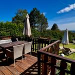 Terrasse mit Tisch, Stühlen und Sonnenschirmen. Blick auf grünen Garten und Wald.