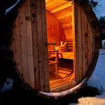 Holzsauna im Schnee mit geöffneter Tür und Sitzbänken im Inneren.