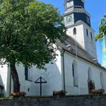 Historische Kirche mit Turm und Blumenbeeten vor Steinmauer.