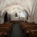 Innenraum einer Kirche mit Holzbänken, gemalten Decken und einem Altarbereich.